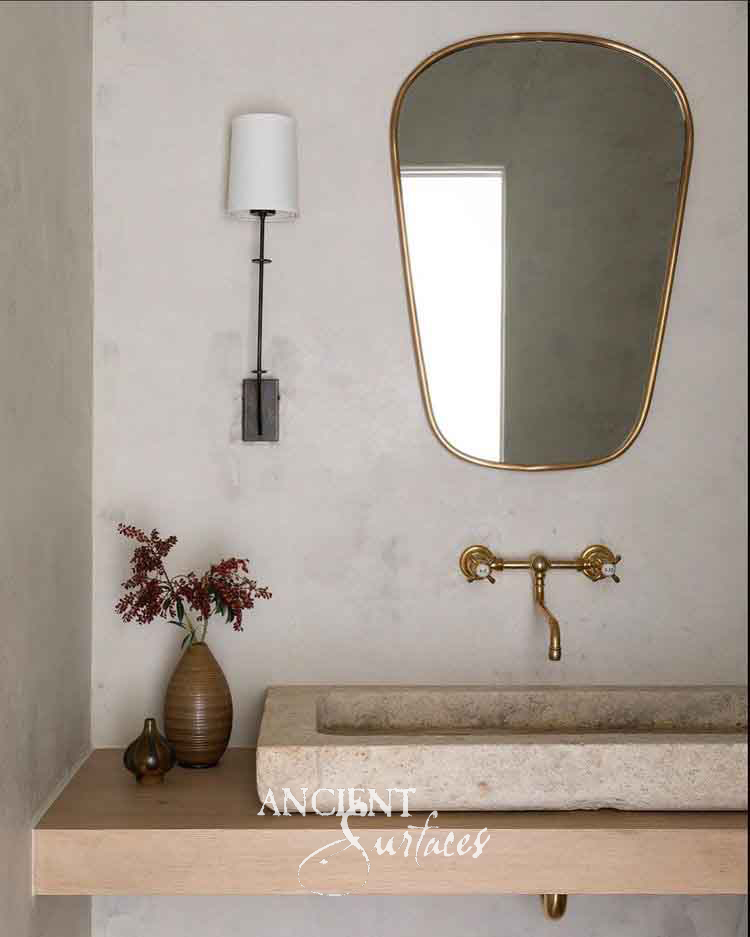 Slim rectangular reclaimed limestone trough sink on a light-oak floating shelf with a brass faucet
