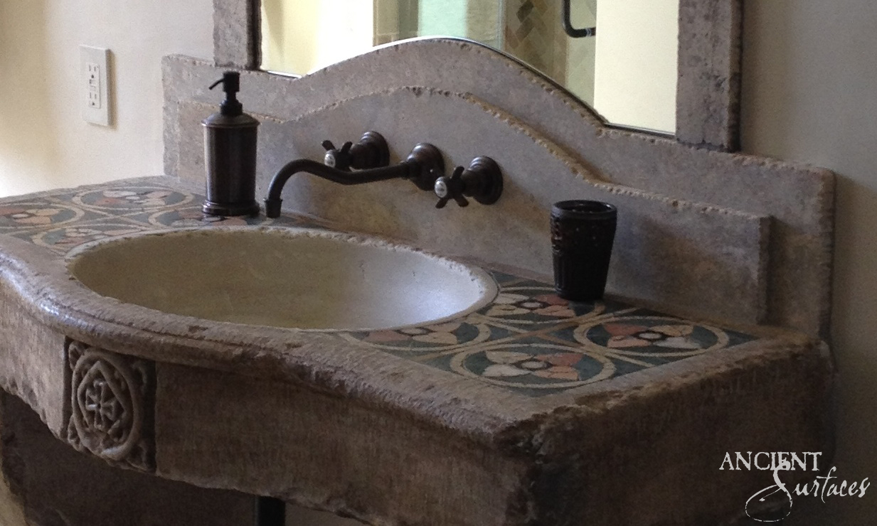 Reclaimed limestone sink with patterned tile-inlaid deck, arched backsplash and carved rosette apron